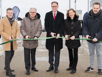 Five people, four men and one woman, in front of a hydrogen filling station, cutting through a green ribbon.
