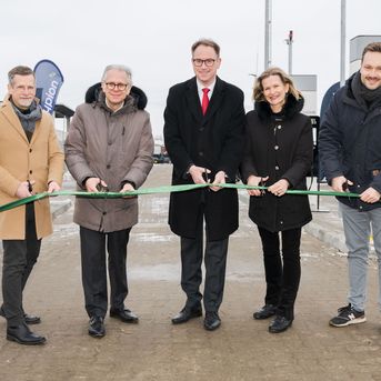 Fünf Menschen, vier Männer und eine Frau, vor einer Wasserstofftankstelle, die ein grünes Band durchschneiden