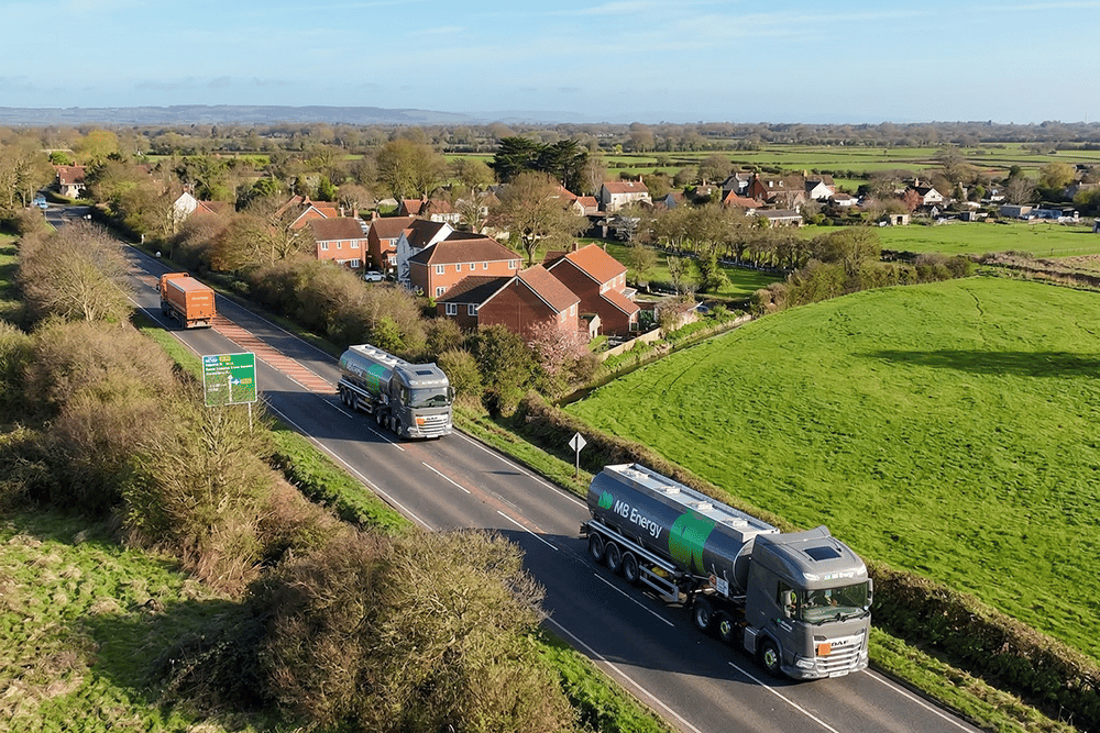 Two MB Energy delivery trucks driving on a street in rural UK