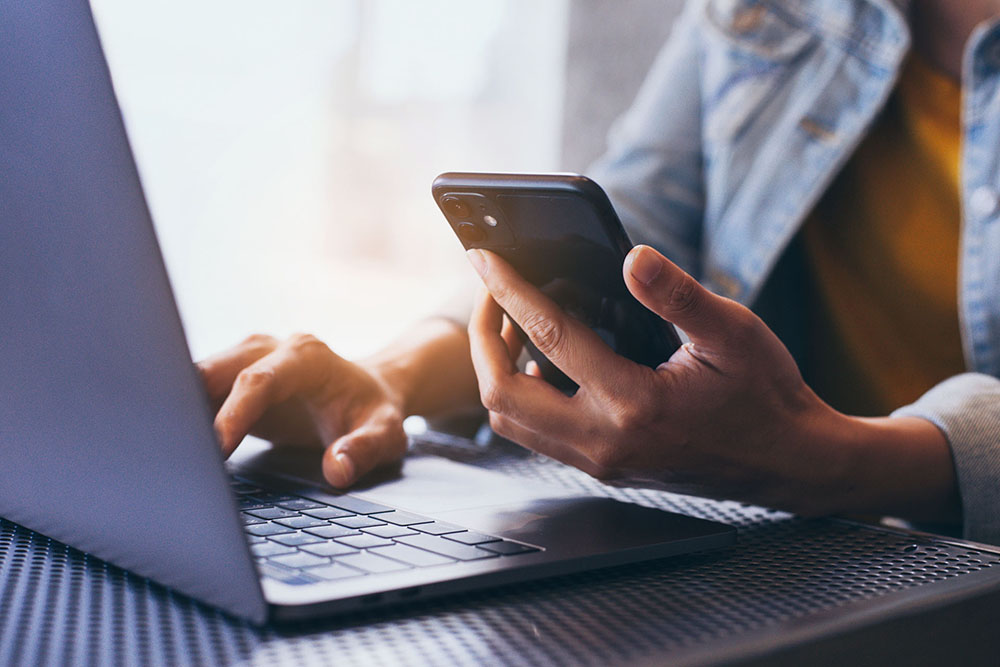 Person berechnet online den aktuellen Heizölpreis mit Smartphone und Laptop